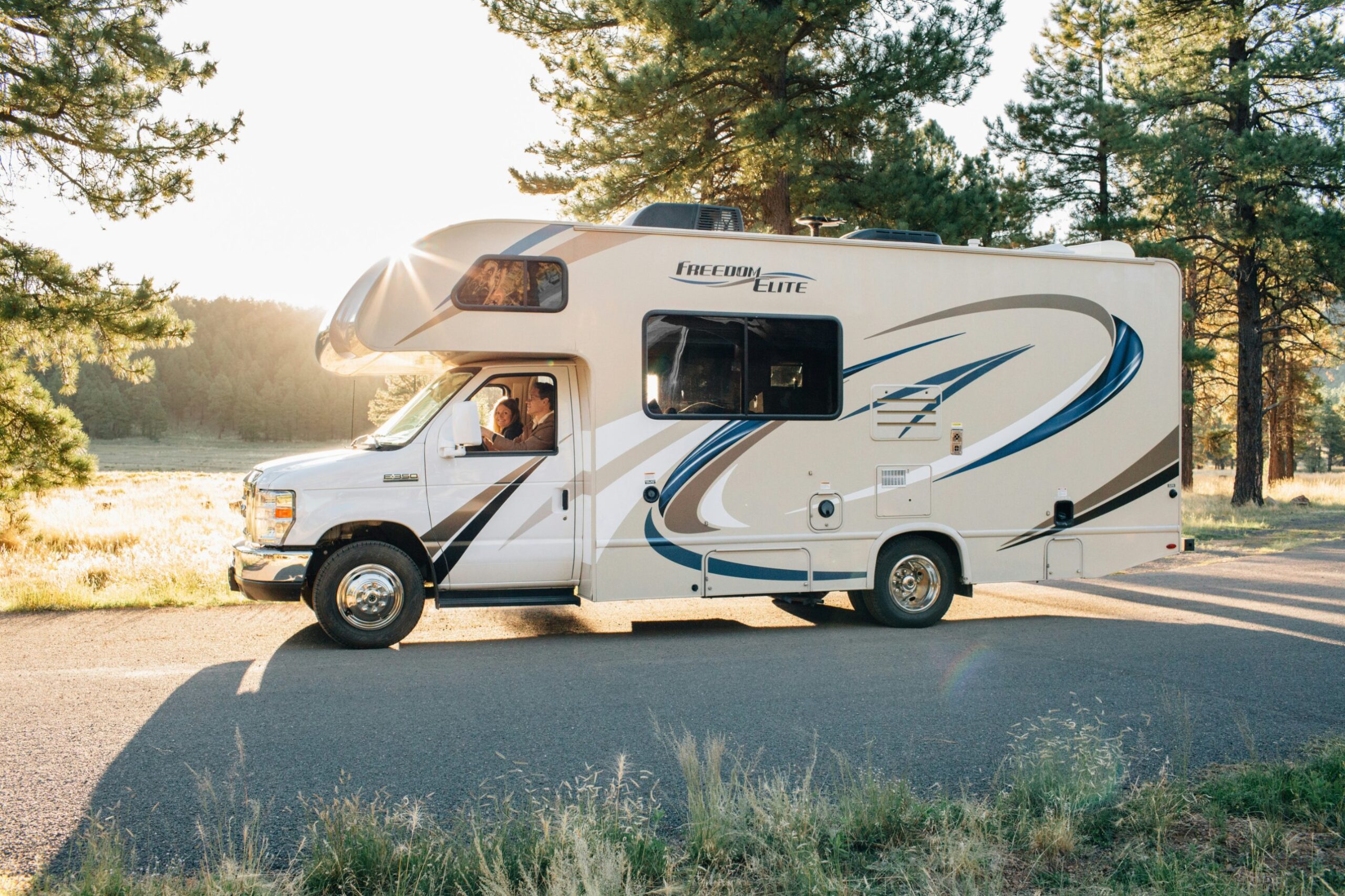 Clean Class C motorhome parked on a forest road at sunrise