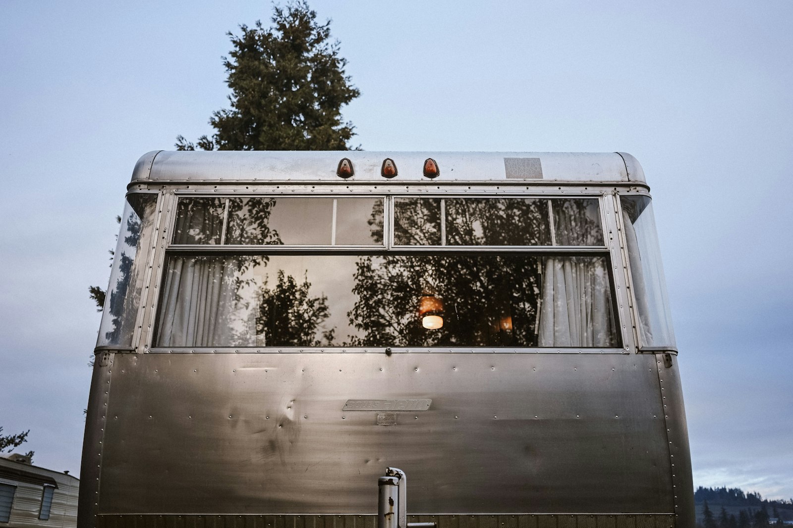 Waxed silver travel trailer with trees reflecting in its polished finish
